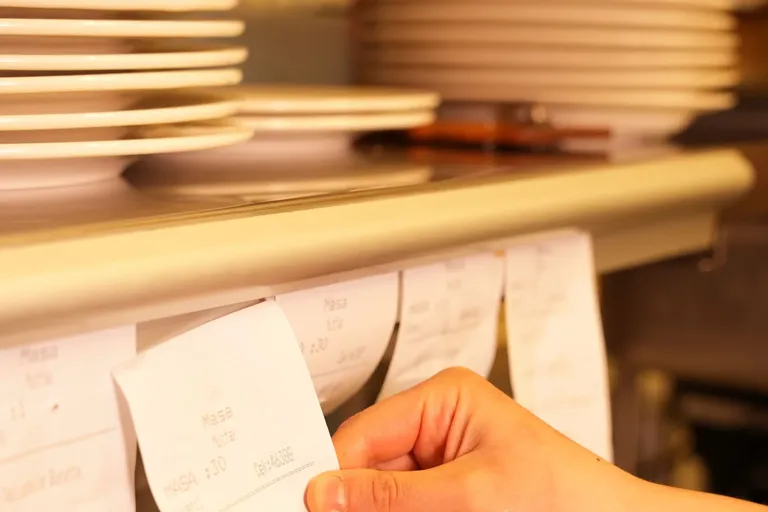 Dłoń zdejmuje papierowy bloczek zamówienia zawieszony w rzędzie w kuchni restauracji