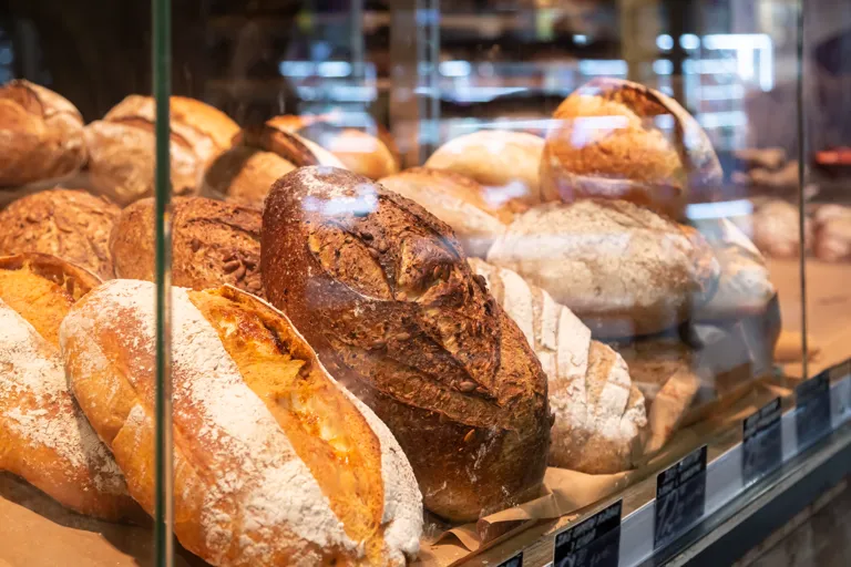 Pieczywo za szklaną witryną piekarni, na półkach bochenki chleba różnych rodzajów