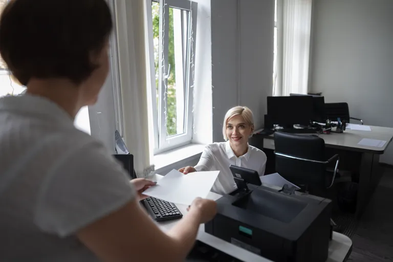 Pracownica biura przyjmuje dokumenty przy stanowisku z drukarką