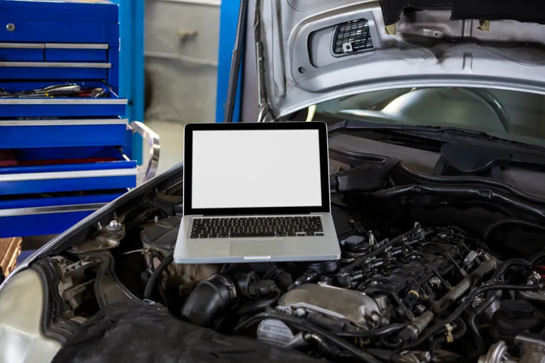 Laptop diagnostyczny umieszczony pod otwartą maską samochodu w warsztacie