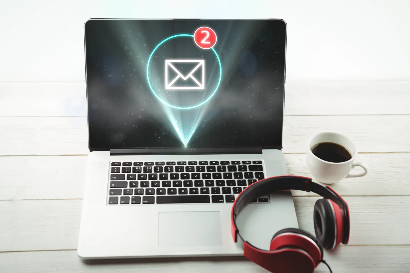 Laptop na biurku z otwartą pocztą internetową, obok kubek kawy i słuchawki