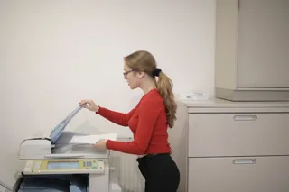 Pracownica biura przy kopiarce z zadrukowaną kartką