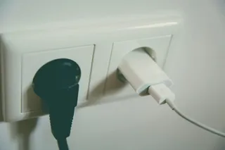 Dwie wtyczki urządzeń wpięte do gniazdka na białej ścianie