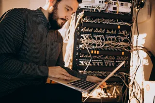 Administrator IT pracuje na laptopie przy szafie serwerowej